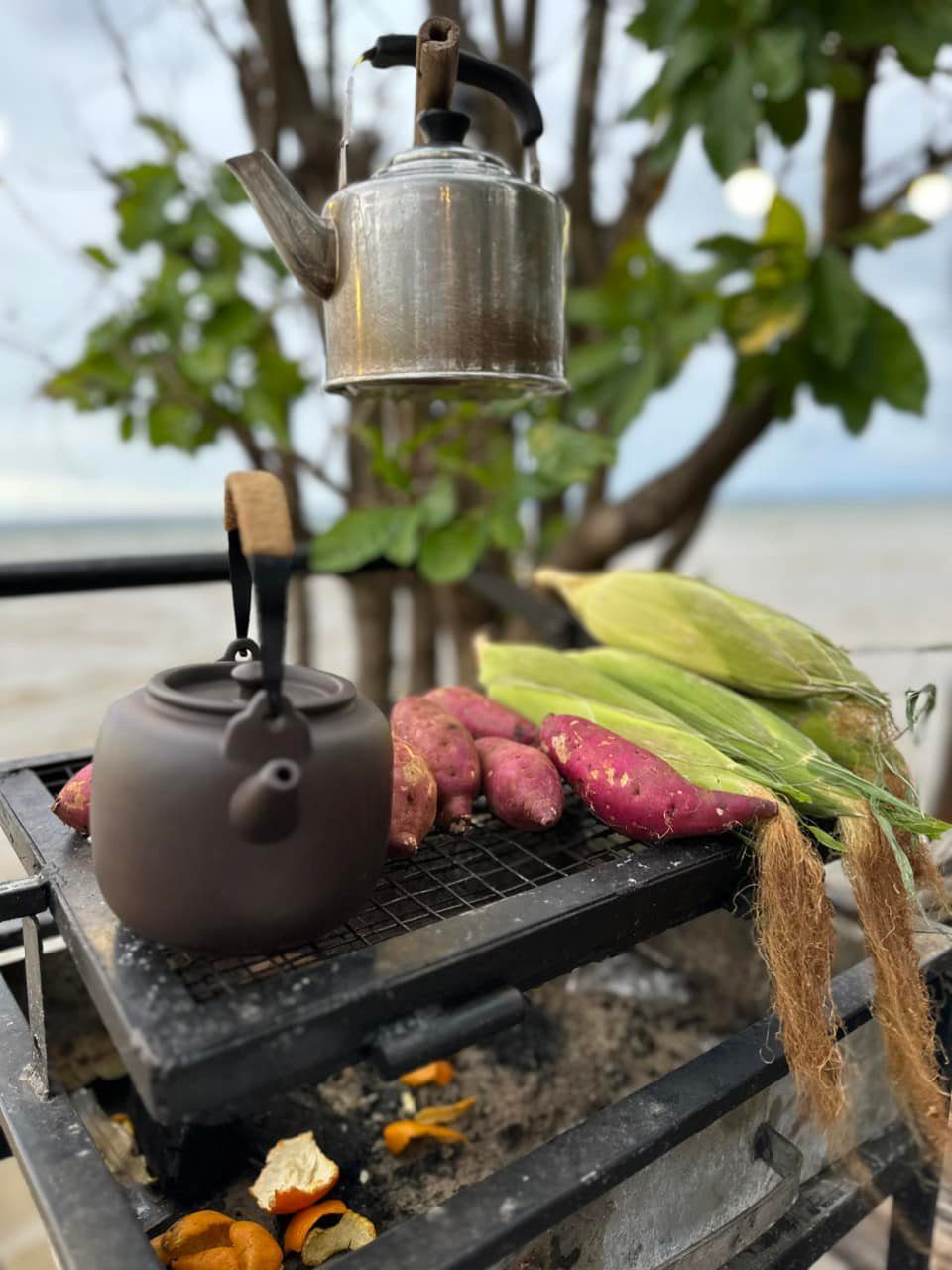 Ấm trà trên bếp than, bắp và khoai chờ nướng, nhìn ra hồ