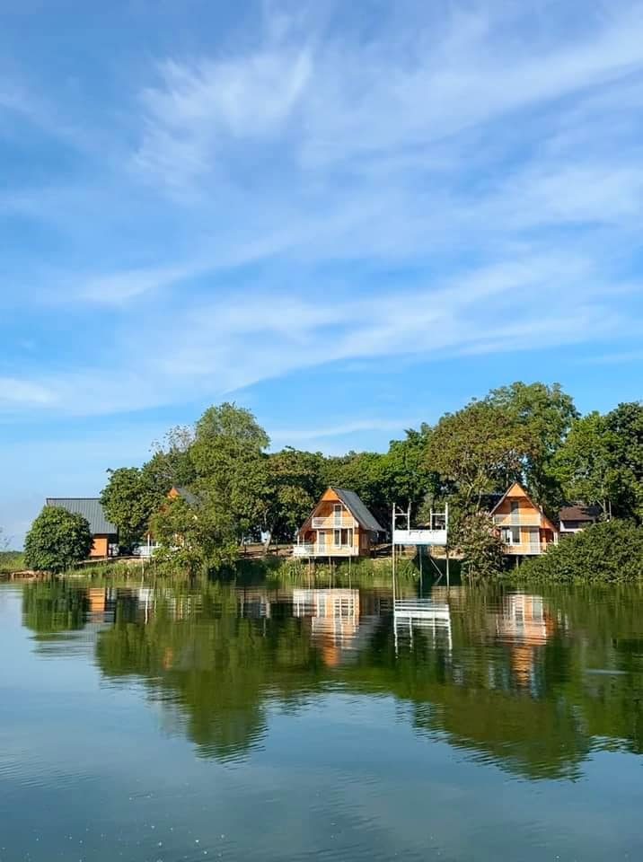 Bờ đảo với dãy nhà mái chữ A giữa cây xanh, nhìn từ mặt hồ