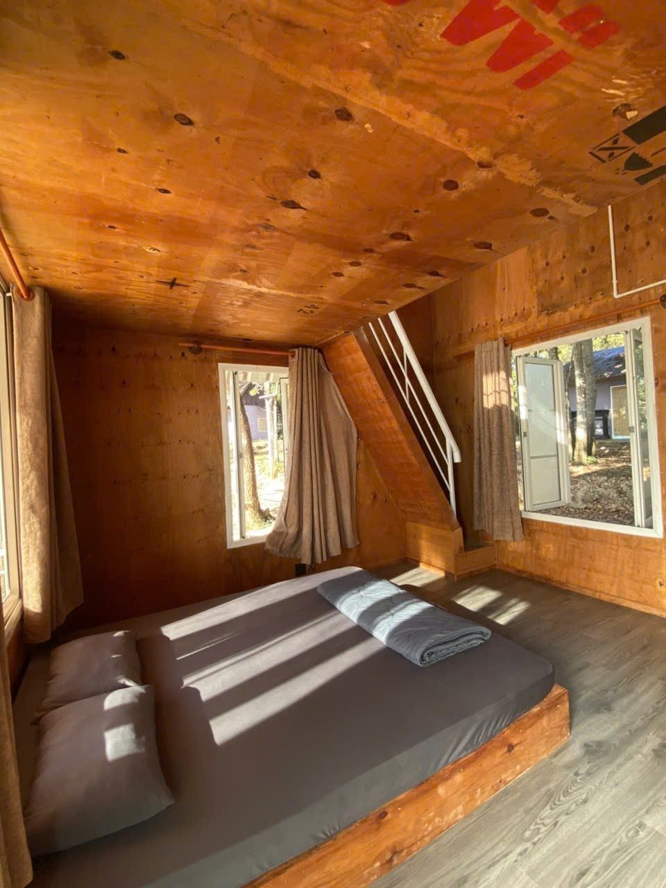 Bên trong bungalow gỗ: hai giường nệm, vách gỗ, cửa sổ sáng
