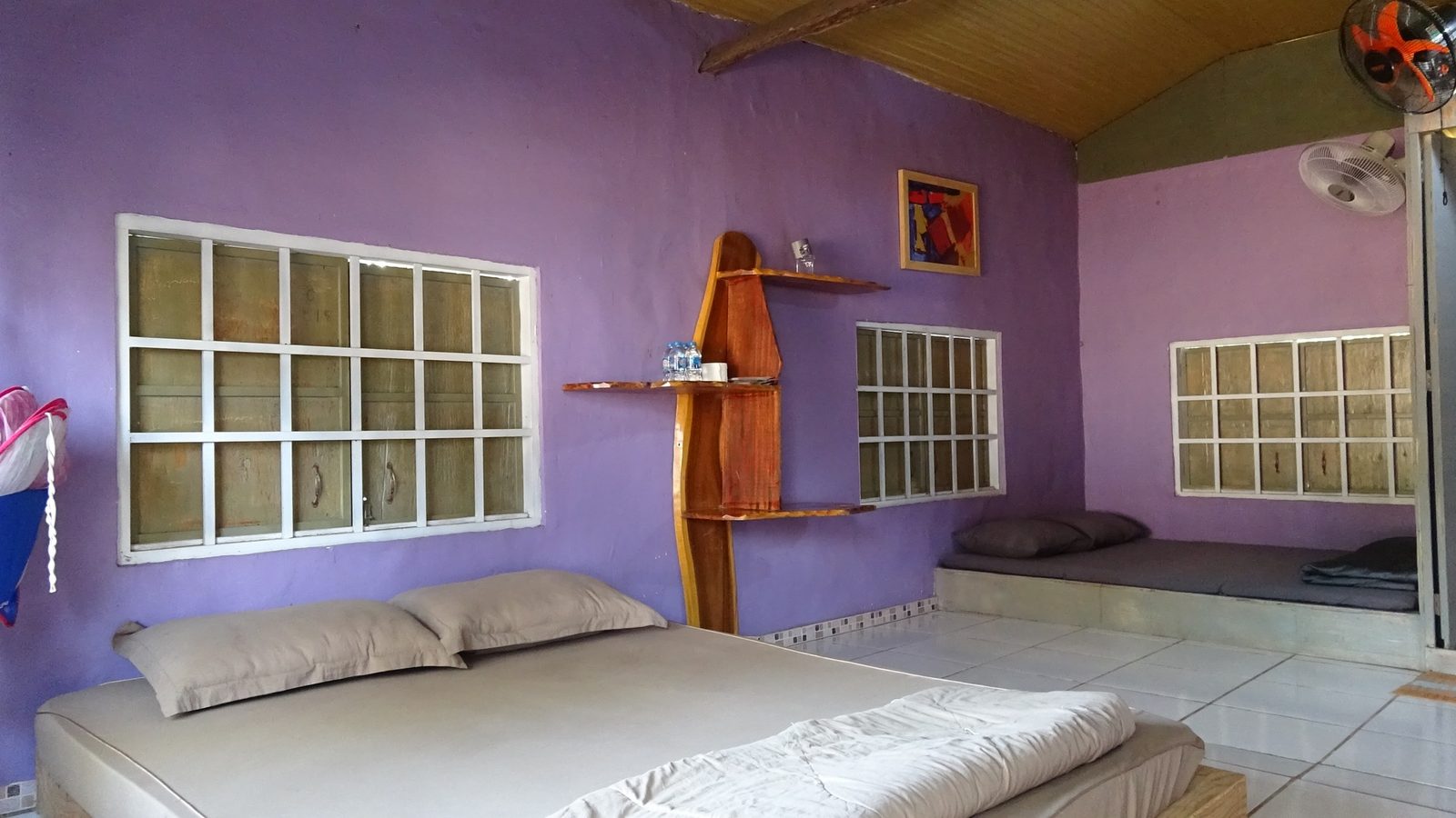 Phòng Homestay Chiều Tím với tường tím, nệm trắng và cửa sổ ô vuông
